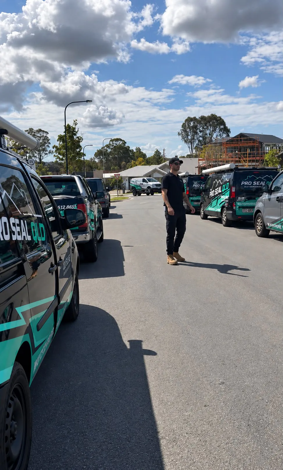 A Pro Seal QLD team member standing between branded utes and vans parked along a new estate street